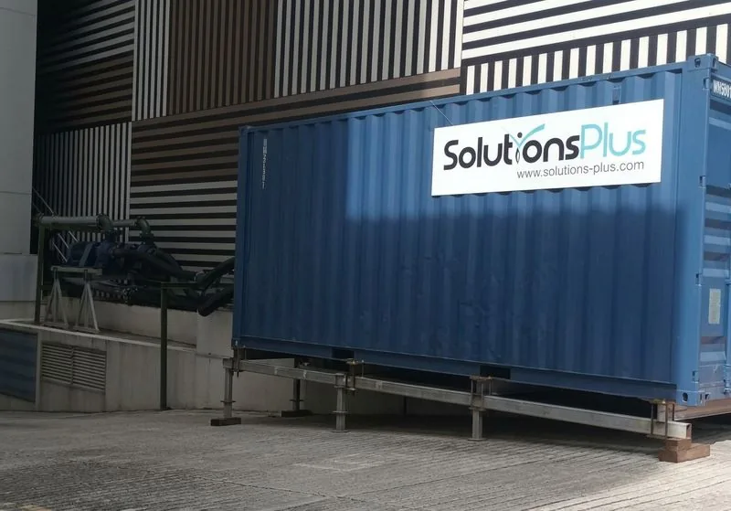 Blue containerised chiller with a Solutions Plus sign beside a building