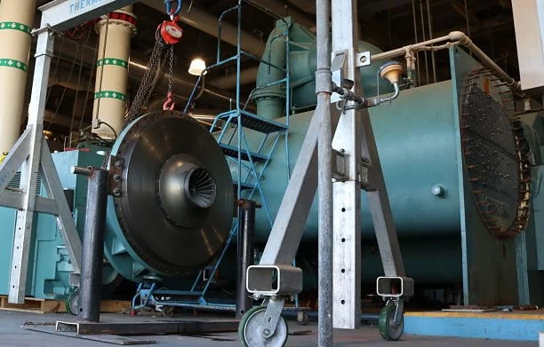 Chiller overhaul in a plant room with the compressor impeller housing removed on a stand beside a teal shell-and-tube vessel